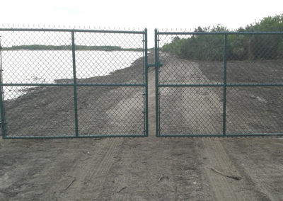 A chain link fence on a dirt road near a body of water.