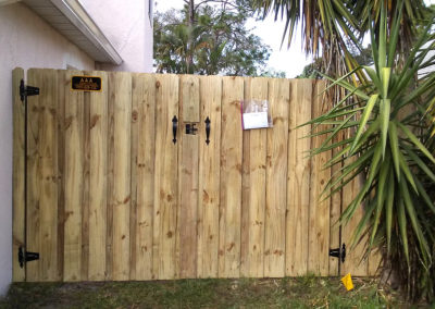 A wooden fence in front of a house with palm trees.